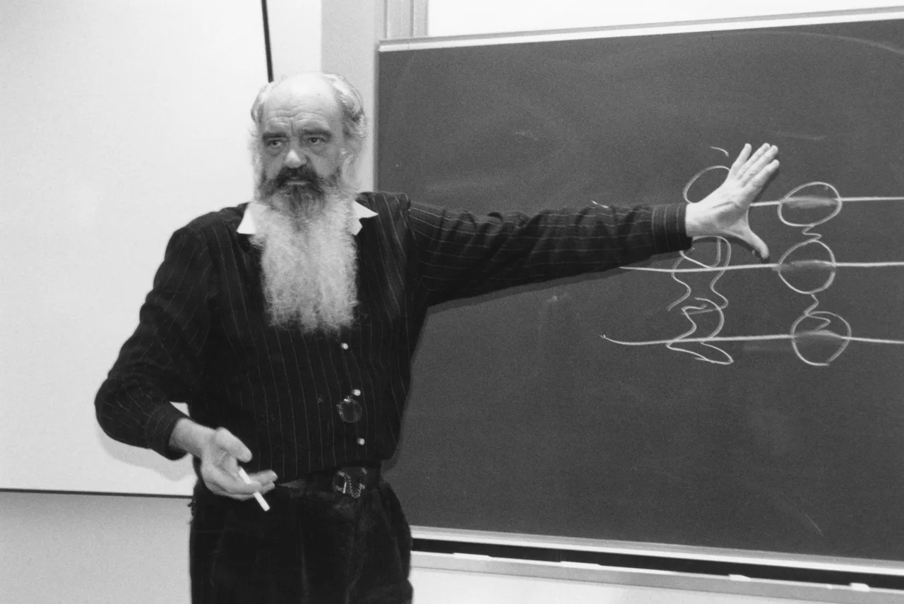 Stafford Beer, con barba larga y blanca, señala un diagrama de círculos dibujado con gis en un pizarrón