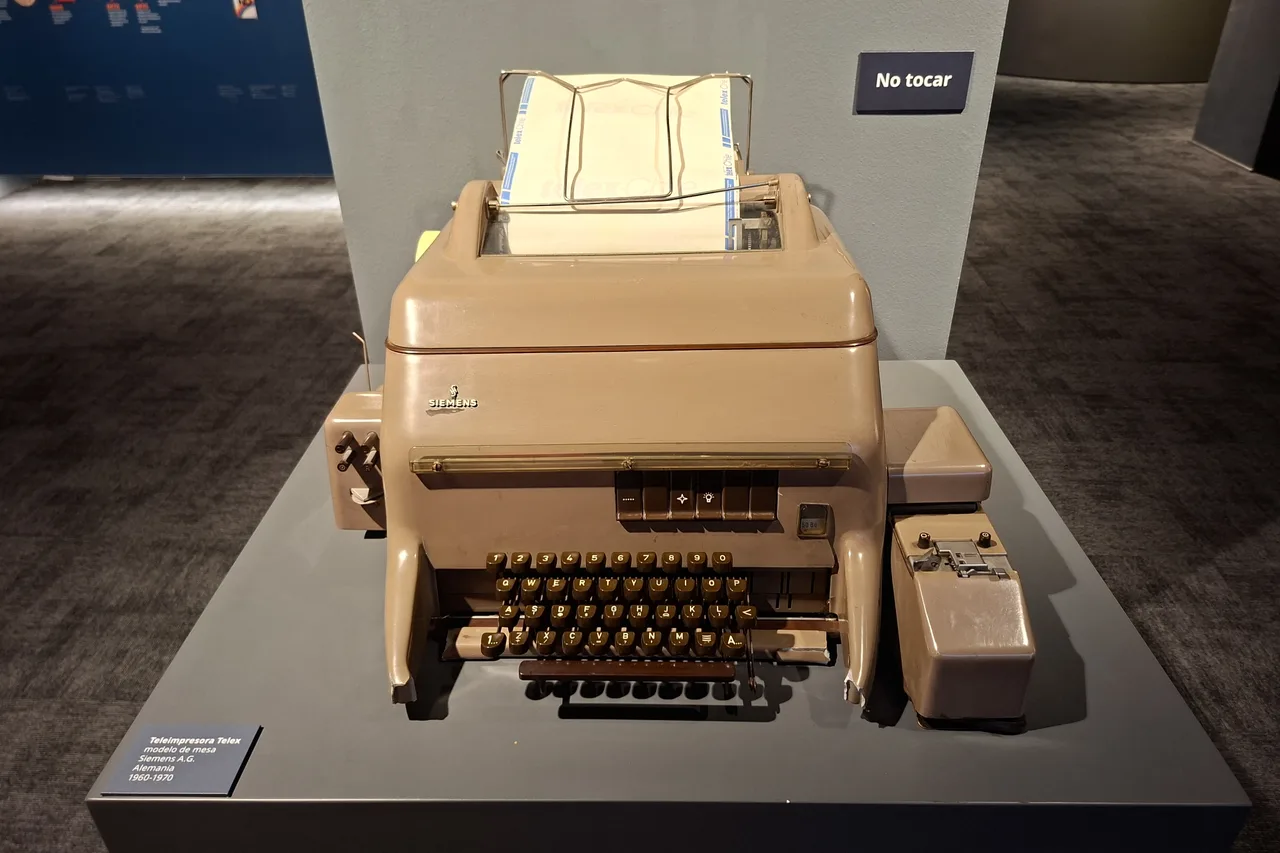 Teleimpresora de télex Siemens color café con teclado y rollo de papel, exhibida sobre un pedestal gris