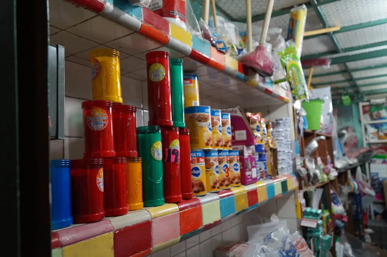Abarrotes hoy Interior de una tienda de abarrotes contemporánea con estantes repletos de productos, veladoras de colores y artículos de limpieza