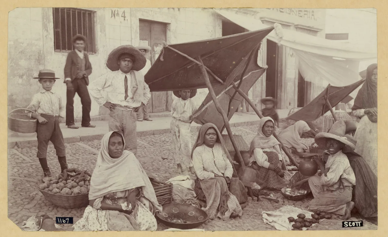 Un mercado, hacia 1900 Fotografía en blanco y negro de un mercado mexicano: puestos con frutas y verduras en el suelo bajo toldos, con vendedores y compradores alrededor