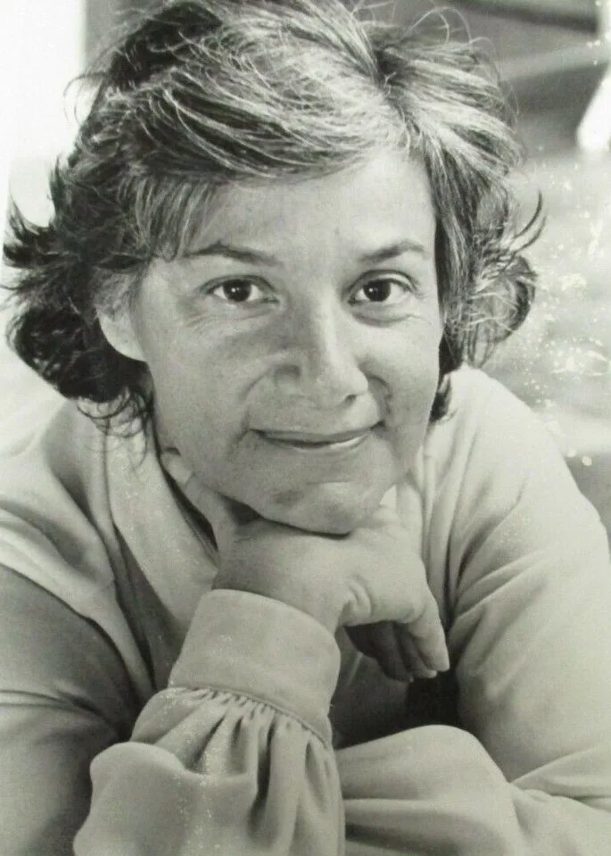 Retrato en blanco y negro de Peggy Charren sonriendo, con la barbilla apoyada en la mano