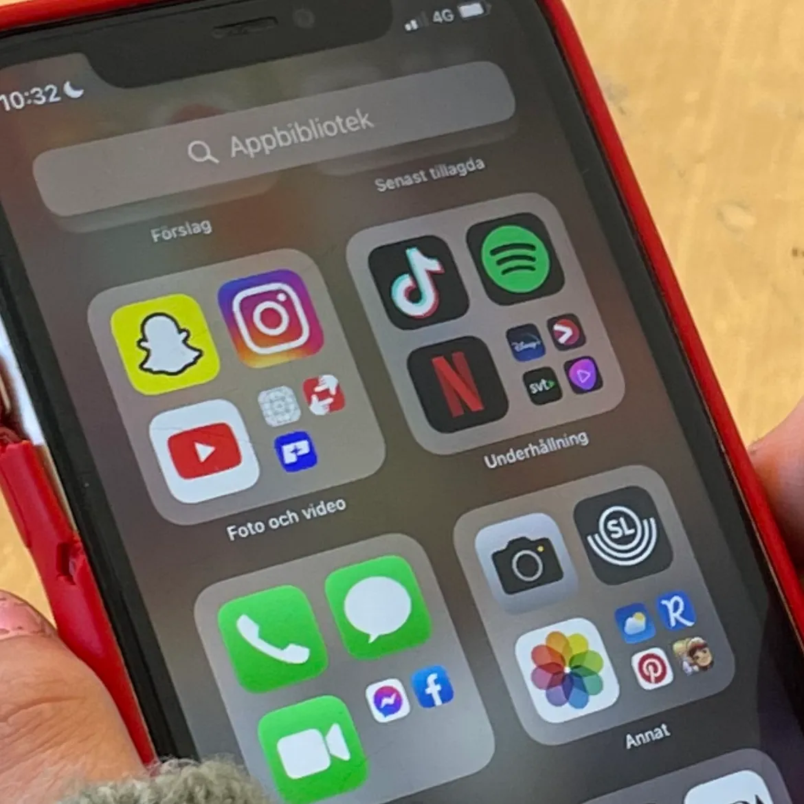 Mano sosteniendo un teléfono con la biblioteca de aplicaciones abierta: TikTok, Instagram, Snapchat, YouTube, Netflix, Spotify y Messenger agrupadas en carpetas