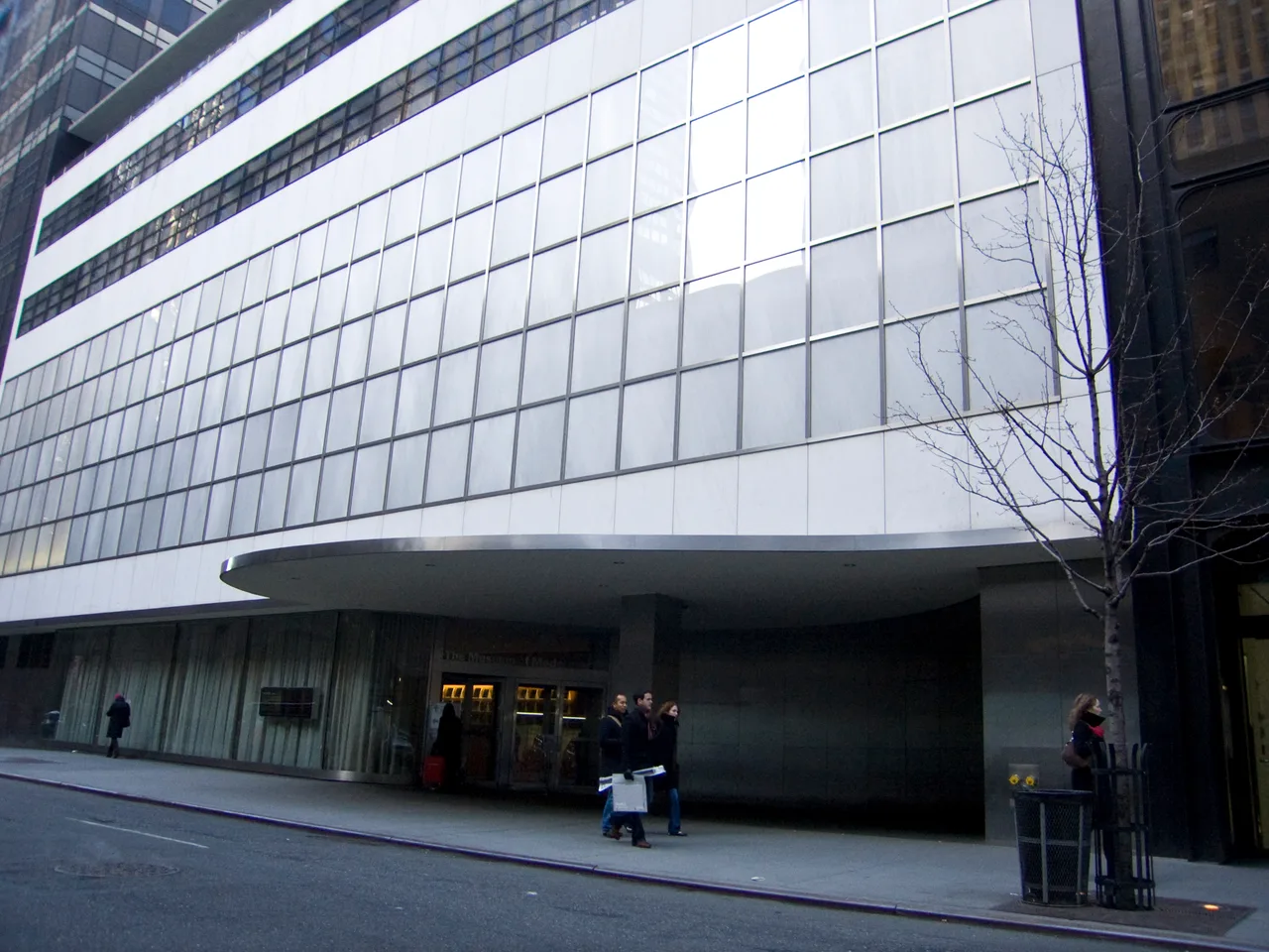 Fachada de vidrio y acero del Museo de Arte Moderno sobre la calle 53 de Manhattan, con peatones en la acera
