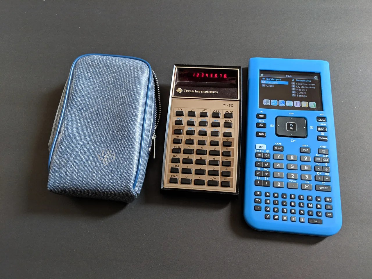 Una calculadora Texas Instruments TI-30 de LED rojo junto a su funda azul y una calculadora gráfica TI-Nspire azul