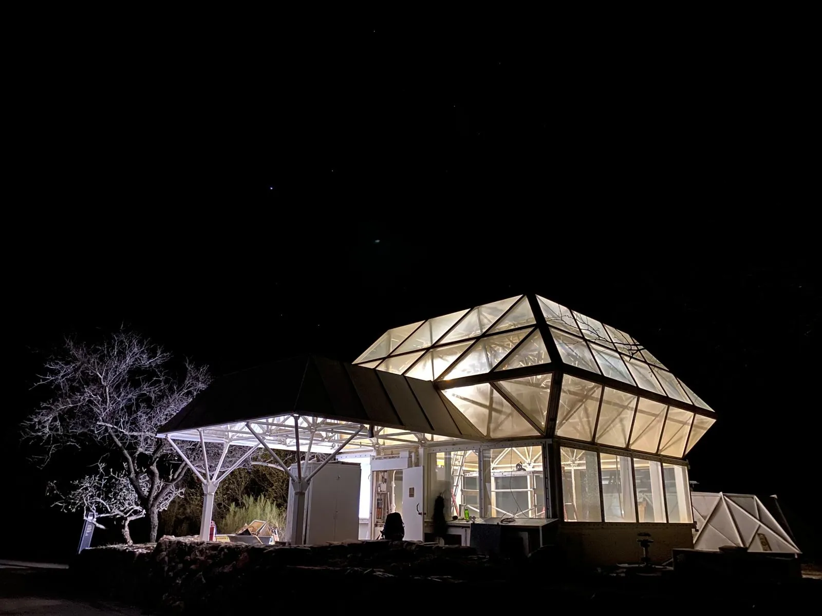 Domo de vidrio iluminado de noche sobre el desierto: el Test Module de Biosfera 2, una estructura facetada con su anexo de techo plano